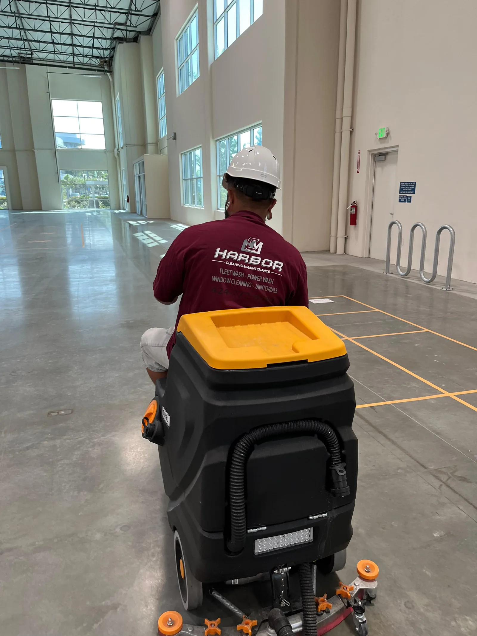 Harbor technician operating a ride-on floor scrubber in a warehouse