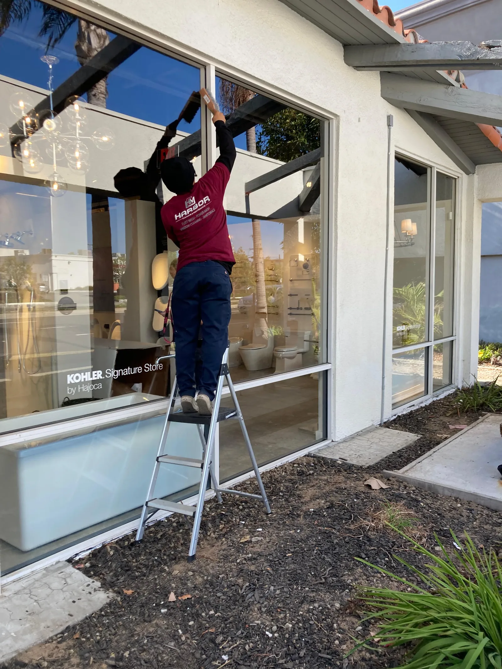 Harbor team member cleaning storefront windows from a ladder